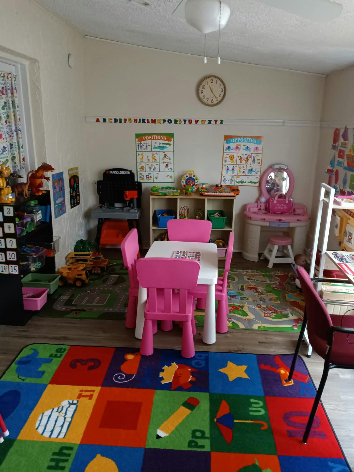 Children's play area with a small table and chairs, toys, and an alphabet rug