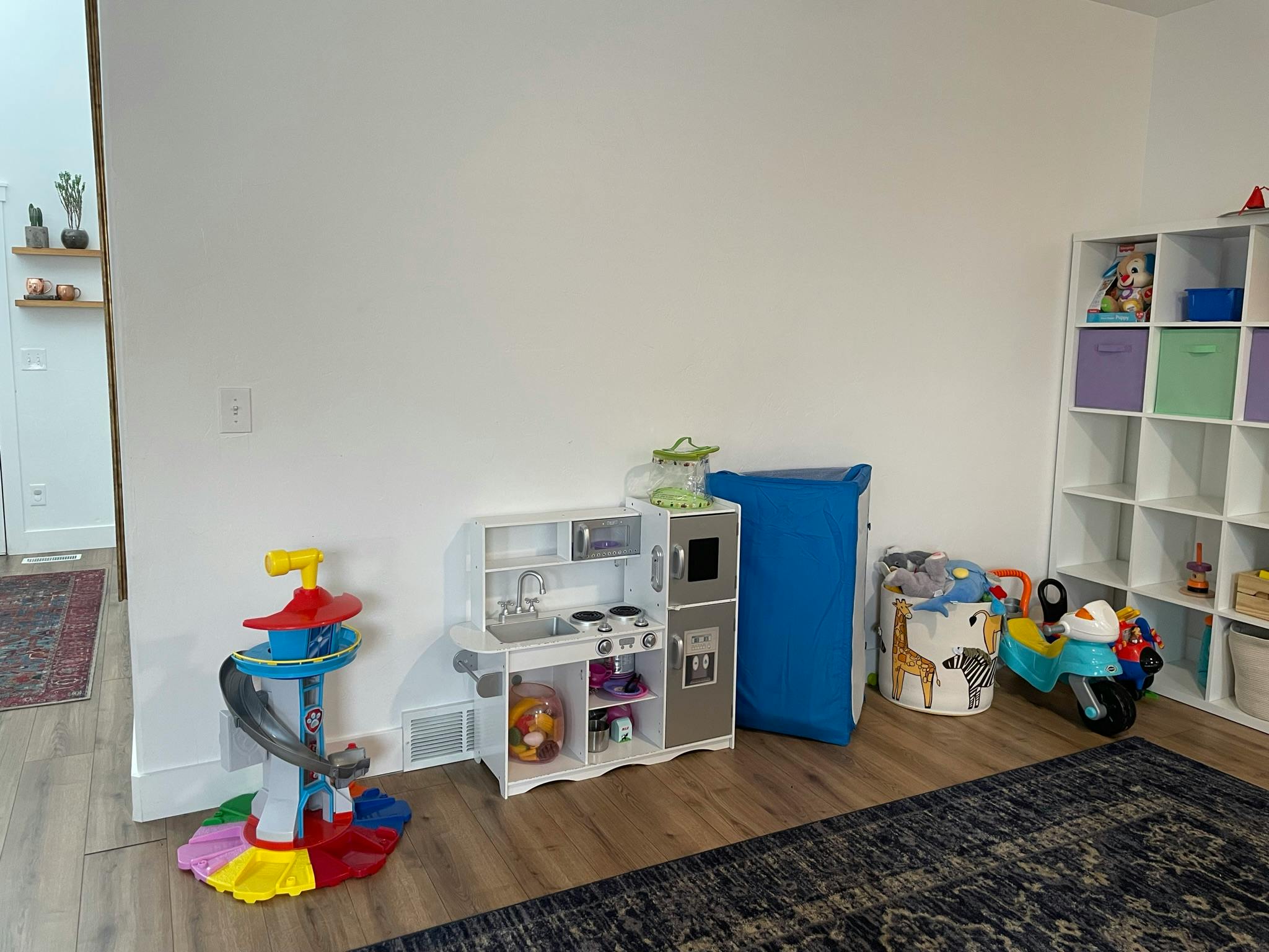 Children's play kitchen, toy car ramp, and storage shelves in a room