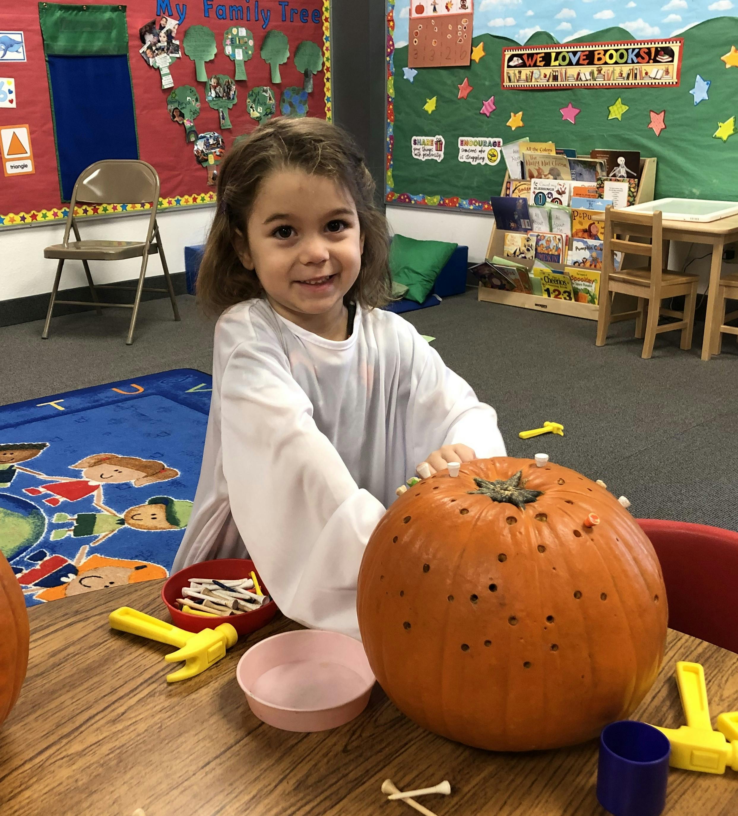 Child decorating a pumpkin with golf tees in a classroom