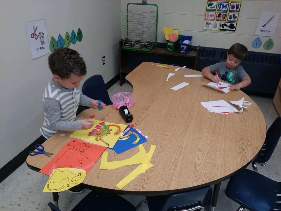 Two children doing crafts at a table in a classroom