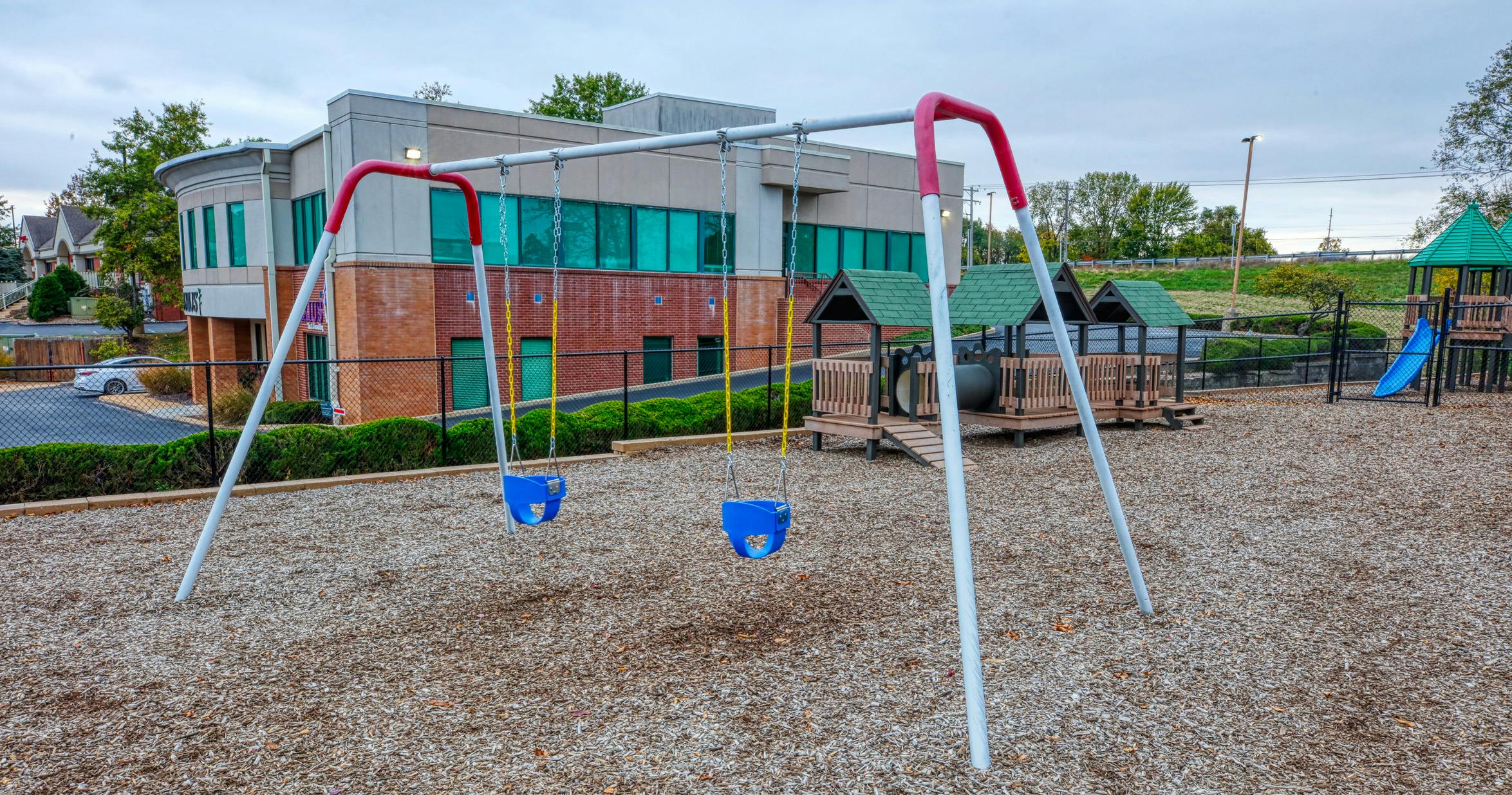 Empty playground with swings and play structures, building in the background