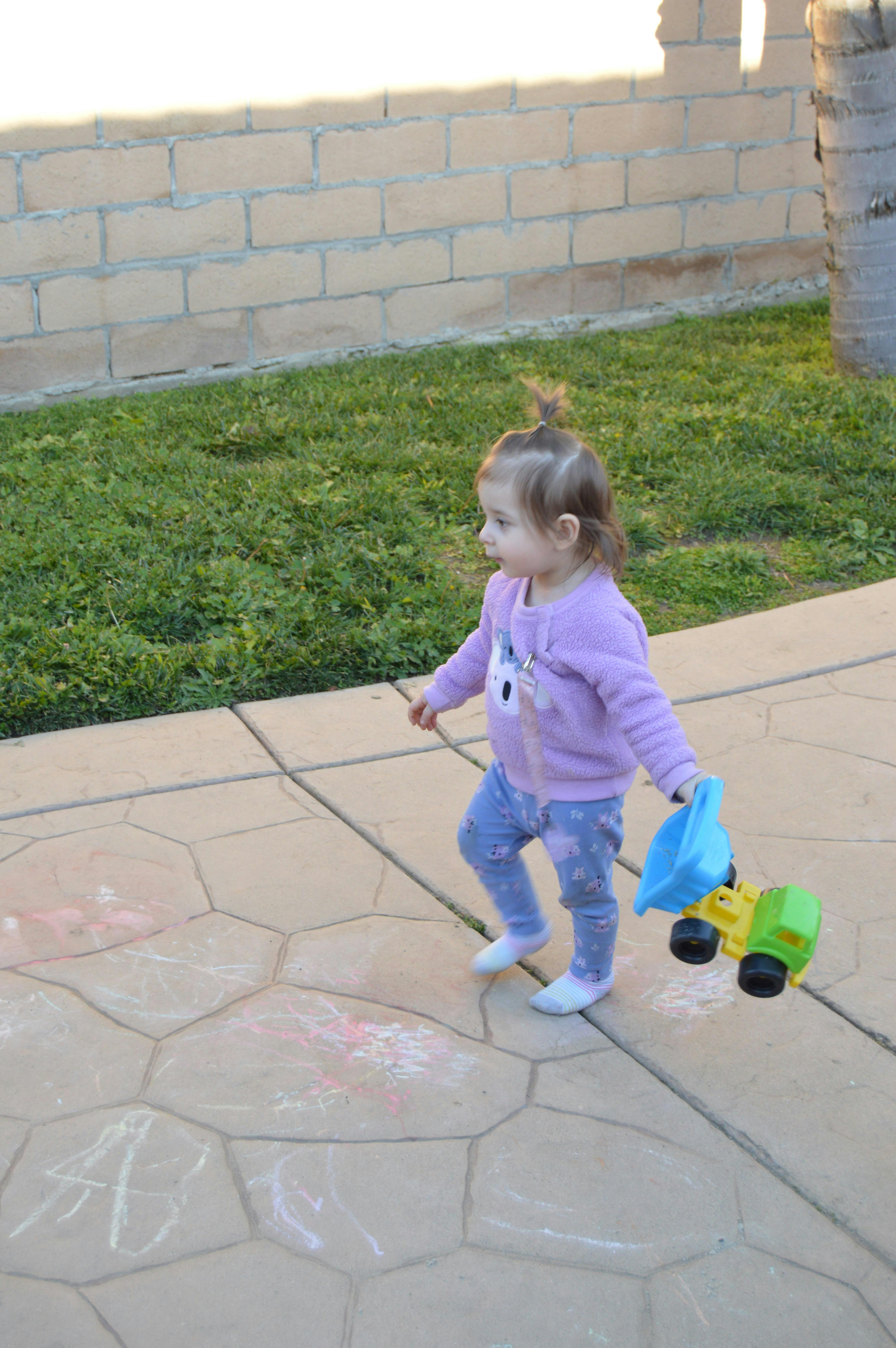 Child walking on a patio holding a toy truck