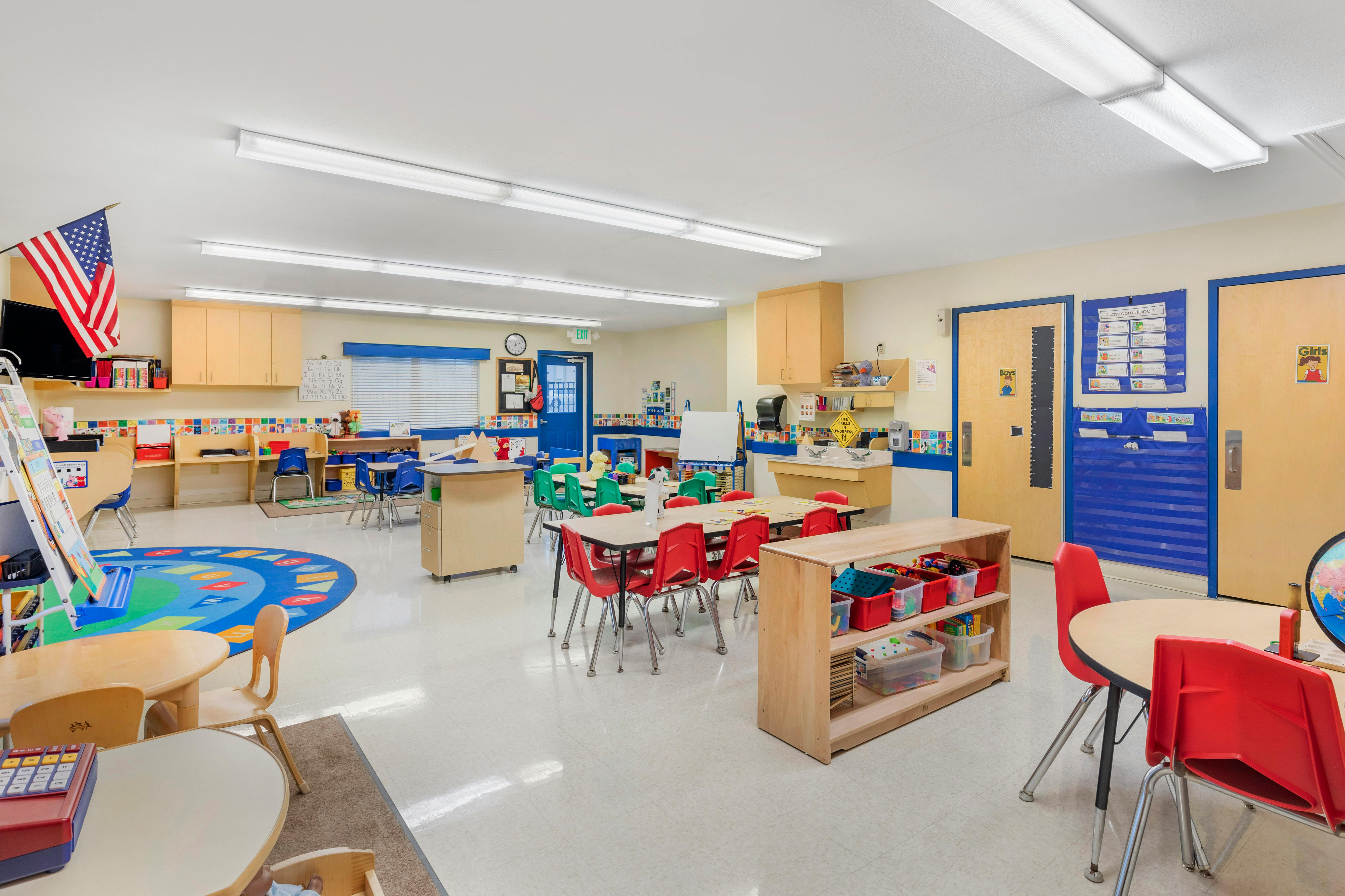 An empty early childhood classroom with small tables and chairs