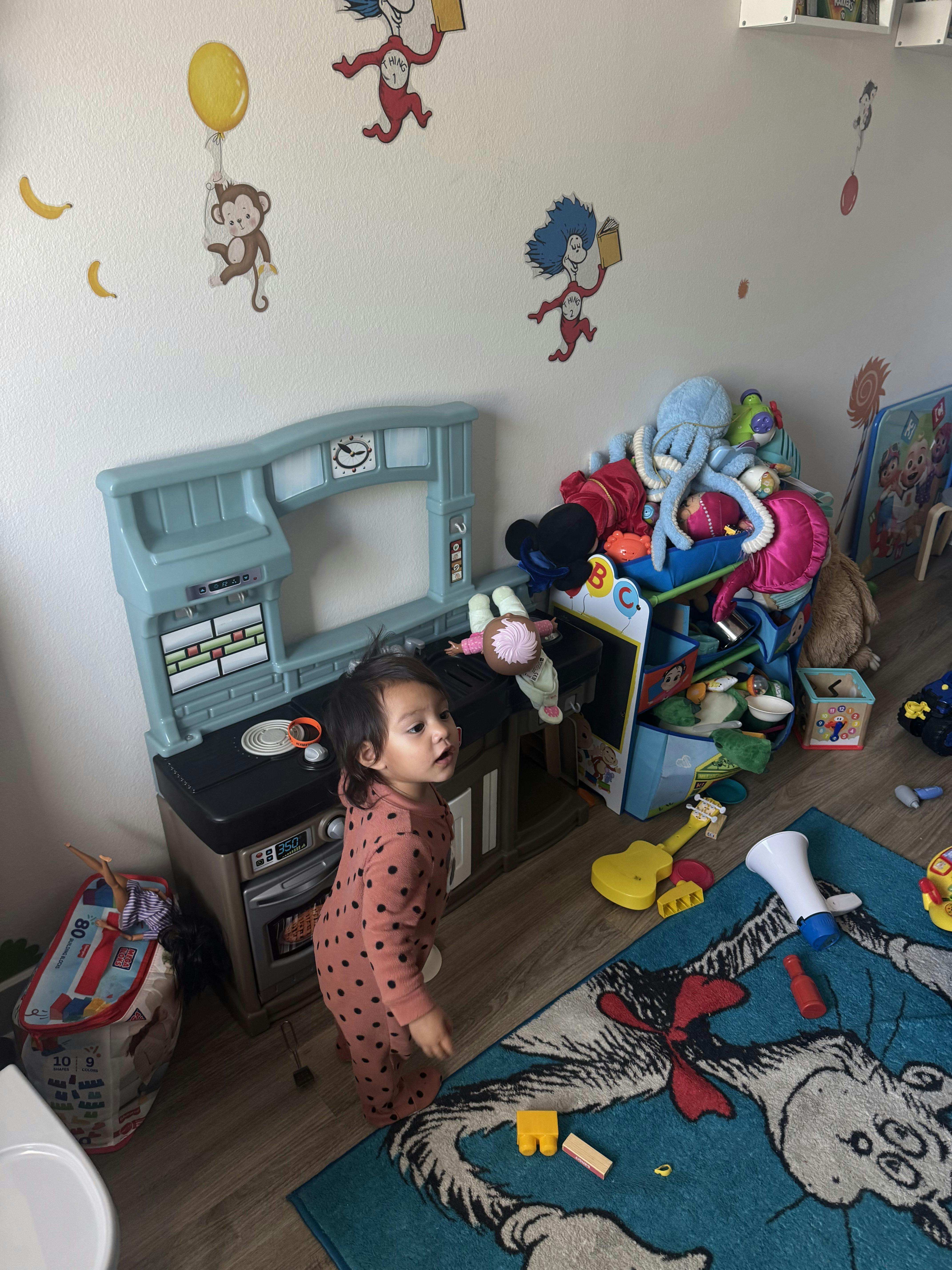 Child standing in a playroom near a toy kitchen and scattered toys