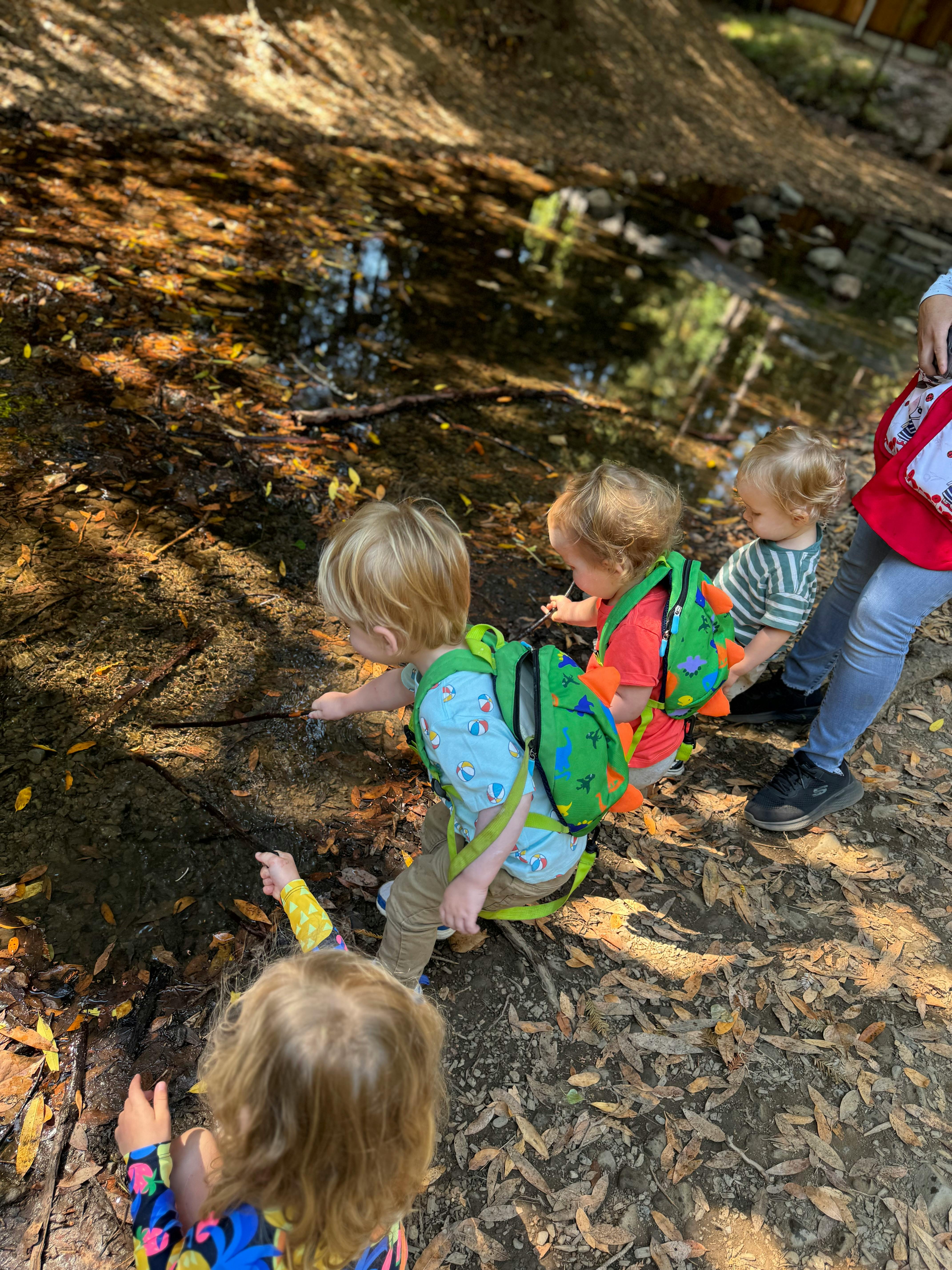 Children with backpacks looking at a muddy puddle
