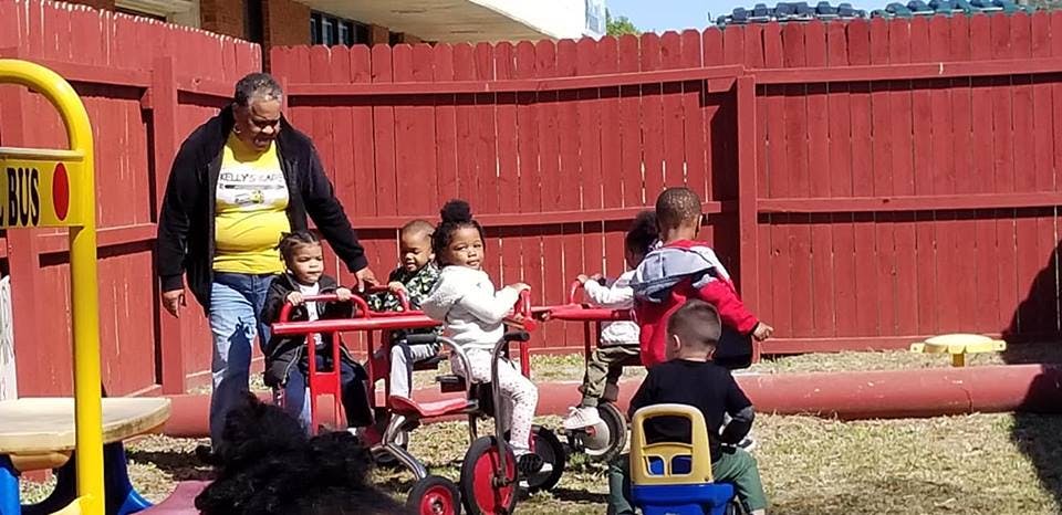 Person with children on tricycles in a fenced outdoor area