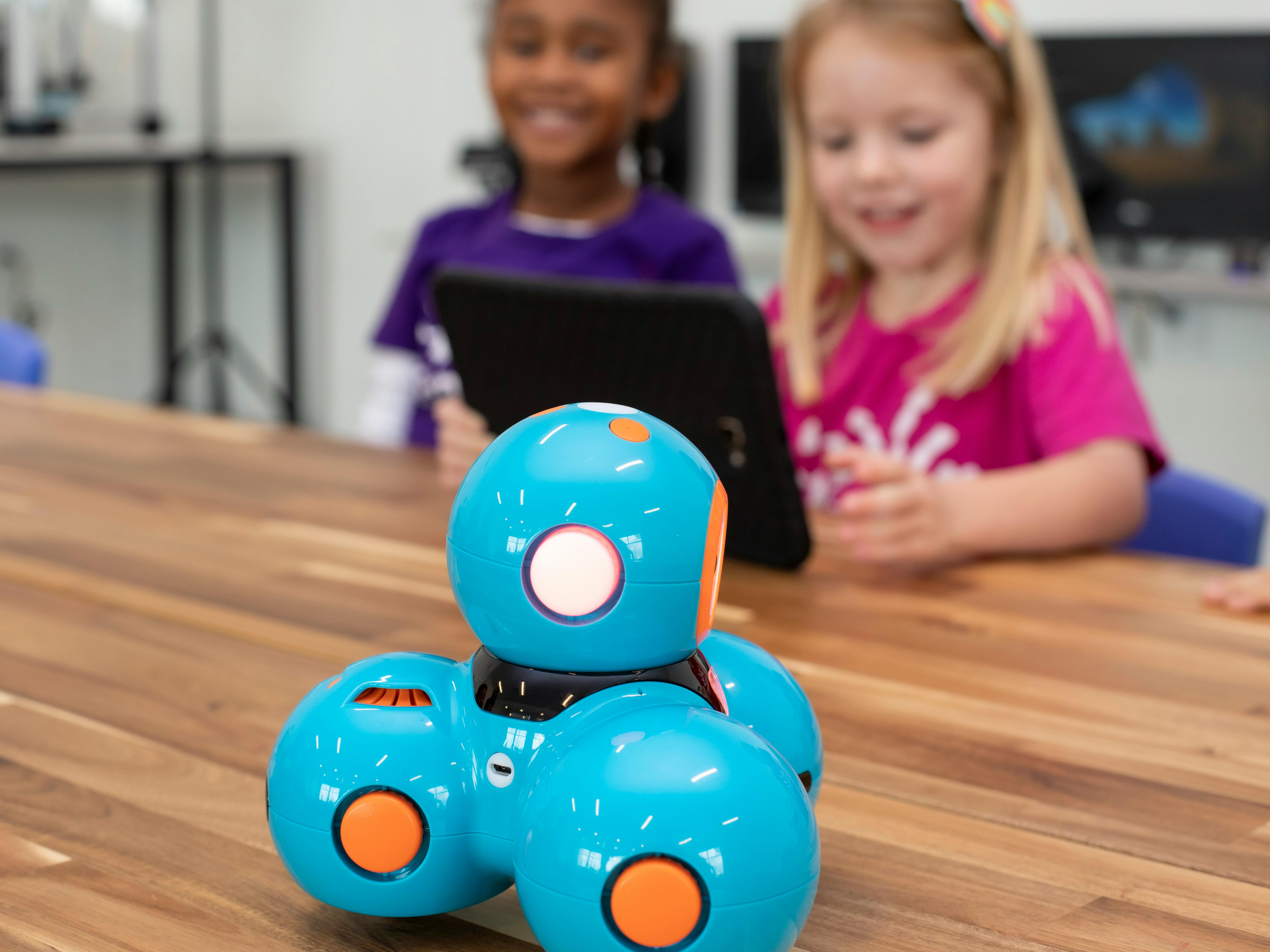 A blue robot with orange accents on a table with two children in the background