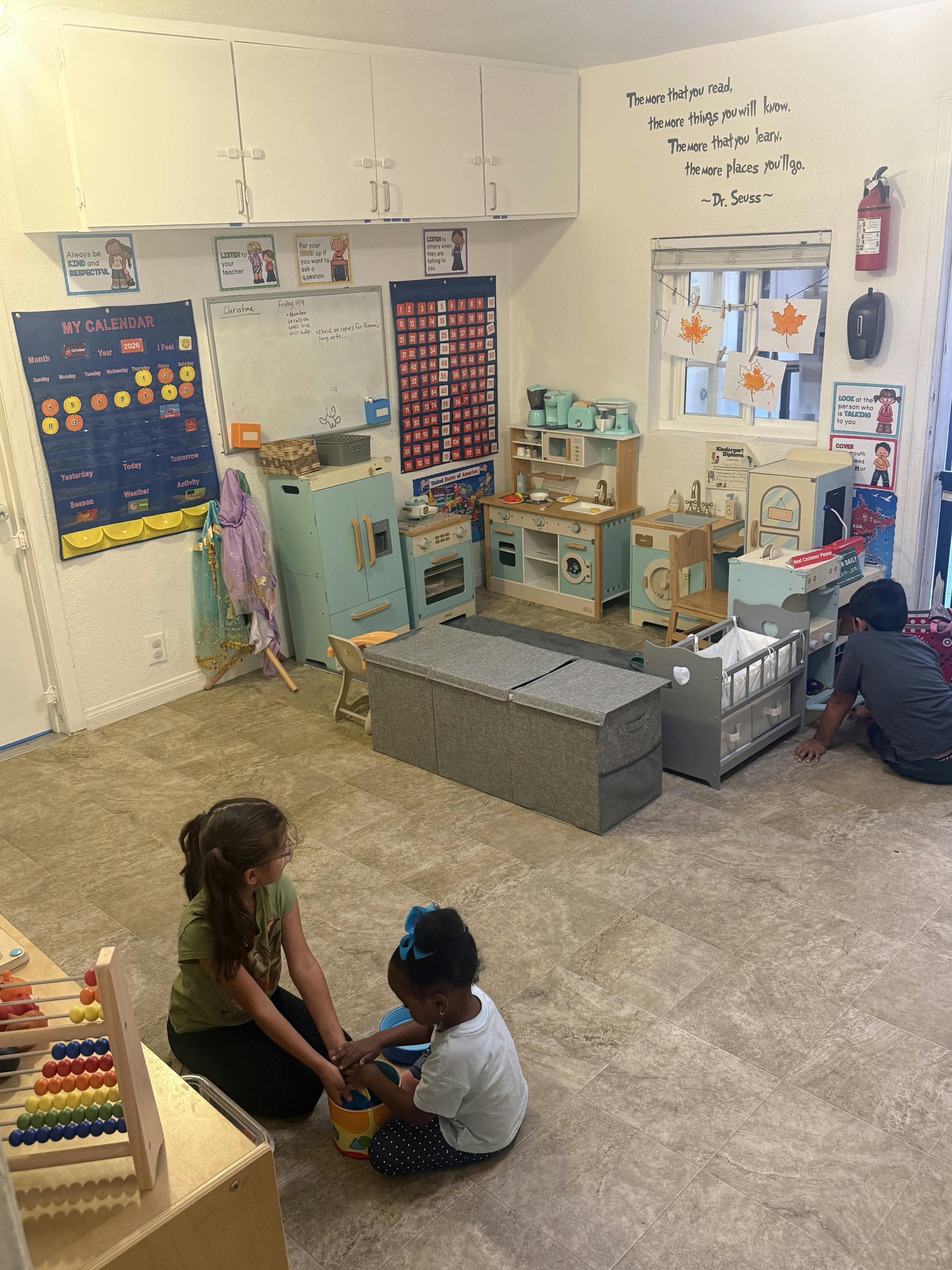 People playing in a classroom with toy kitchens and educational wall charts