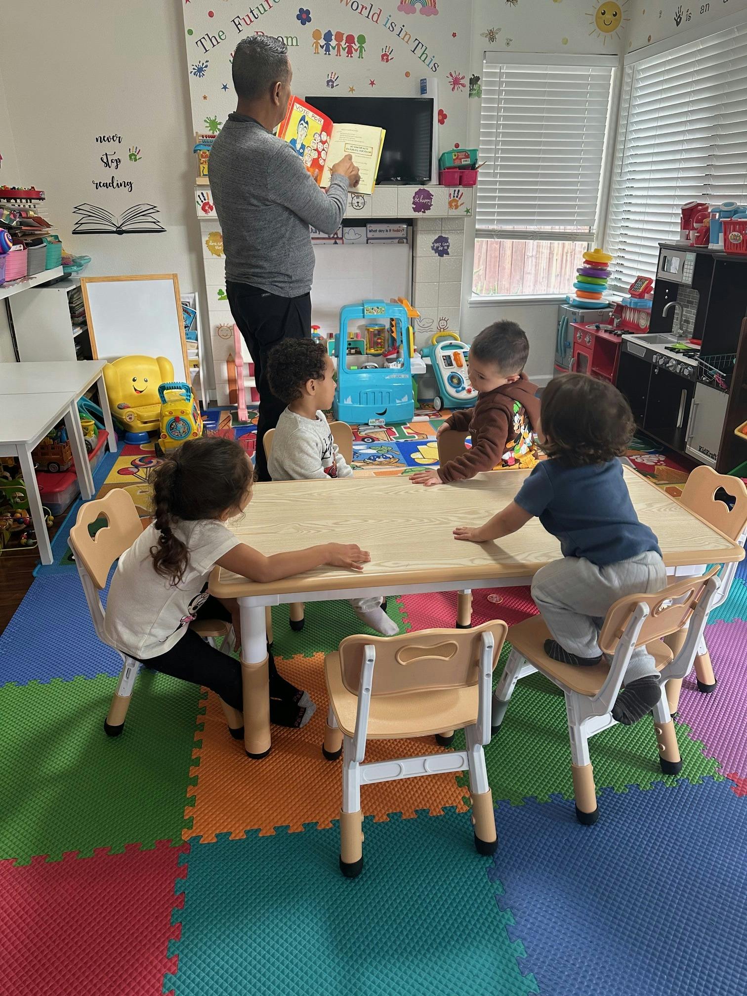 Person reading a book to four children in a classroom