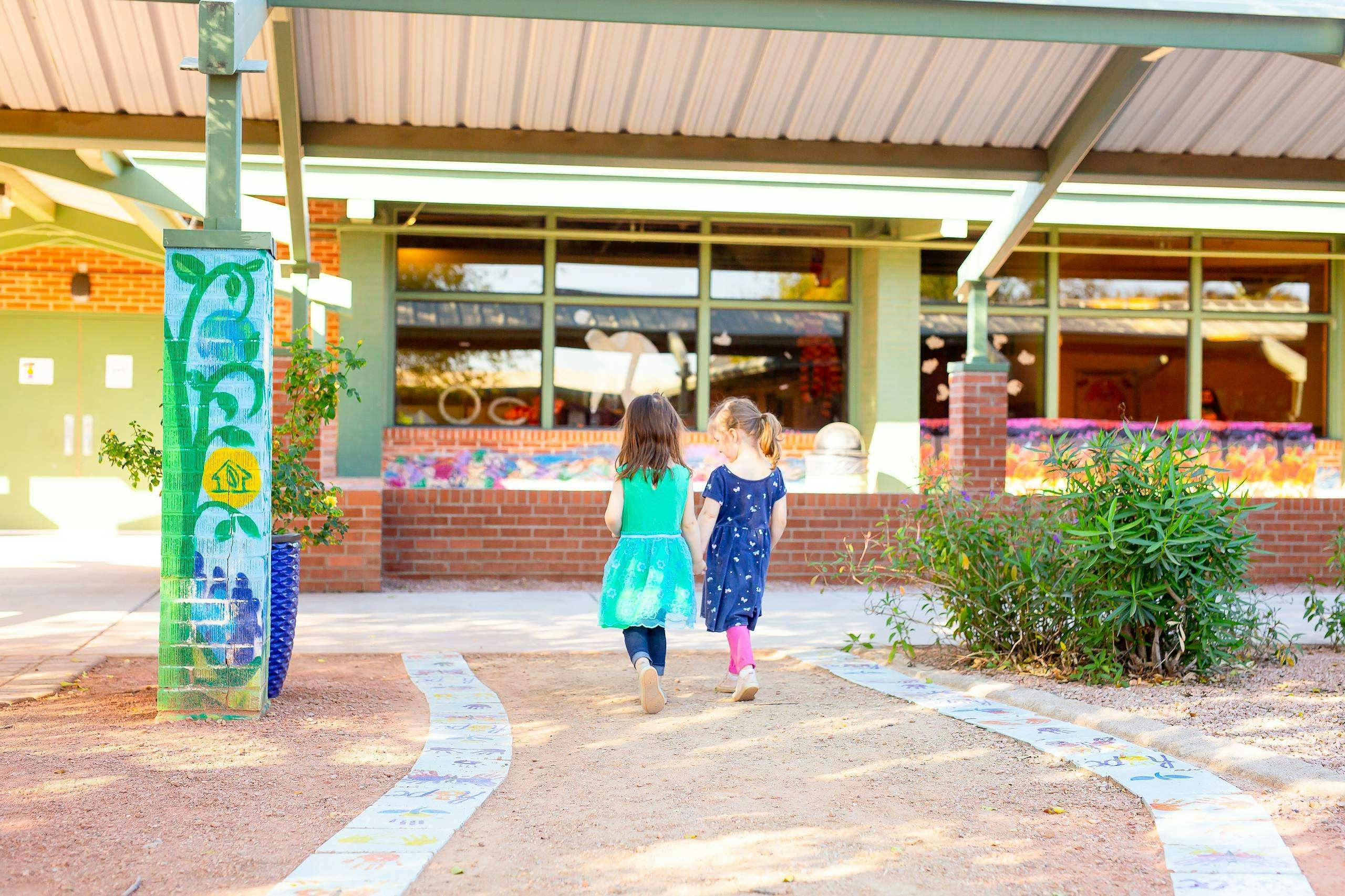 Two children holding hands walking toward a school building