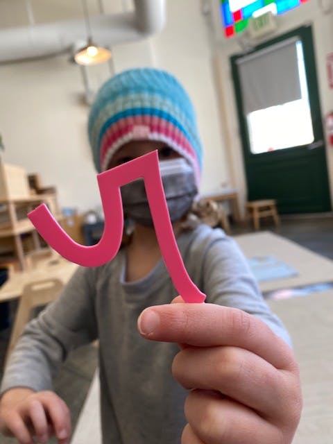 Child in a mask holding up a pink cutout shape