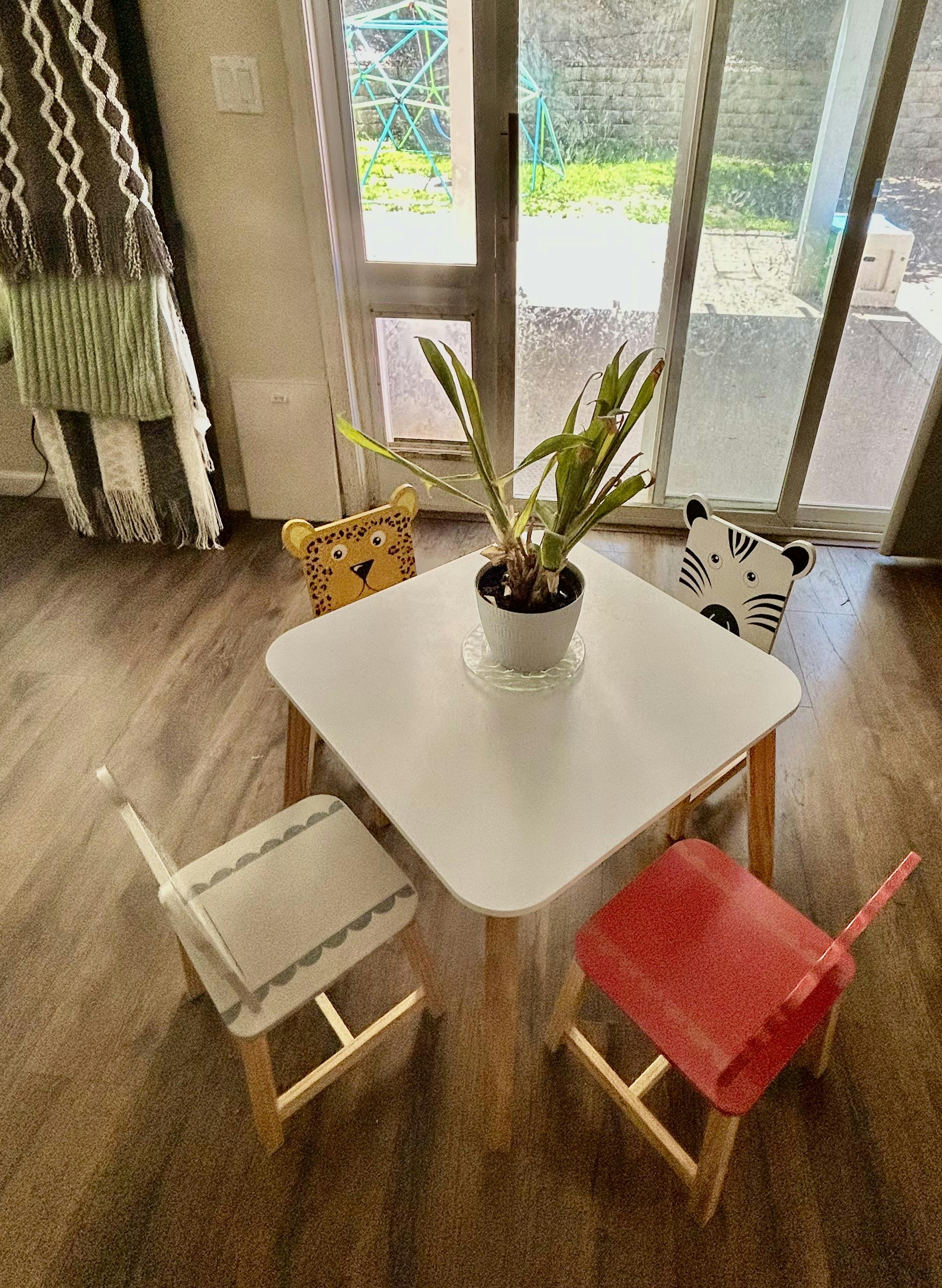 Small white table with a plant and four chairs facing outwards, two with animal faces
