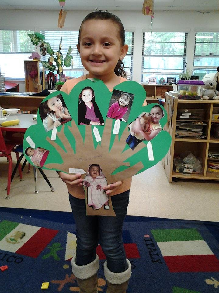 Child holding a paper cutout of a tree with photos of children on it