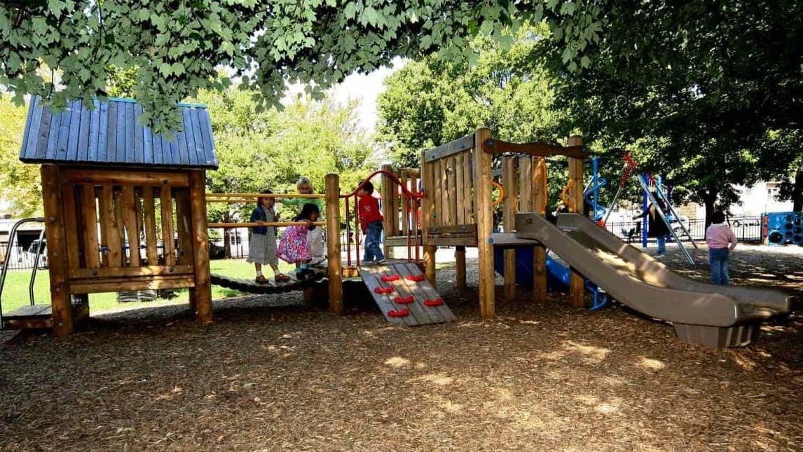 Children playing on a wooden playground structure with slides and climbing structures