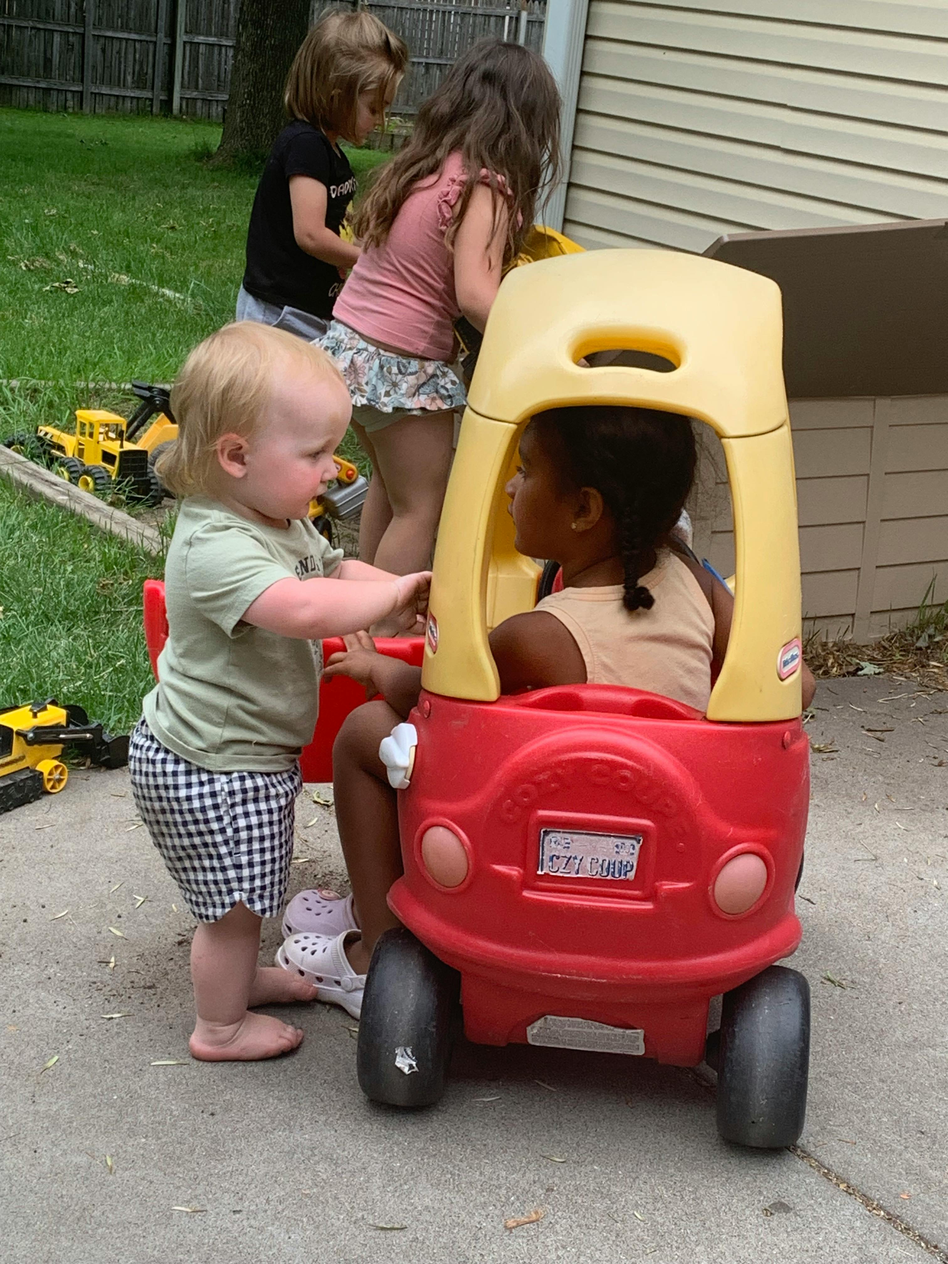 Children playing with a plastic toy car on a paved area