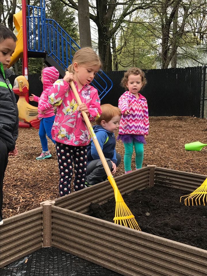 Child raking soil in a raised garden bed with other children nearby