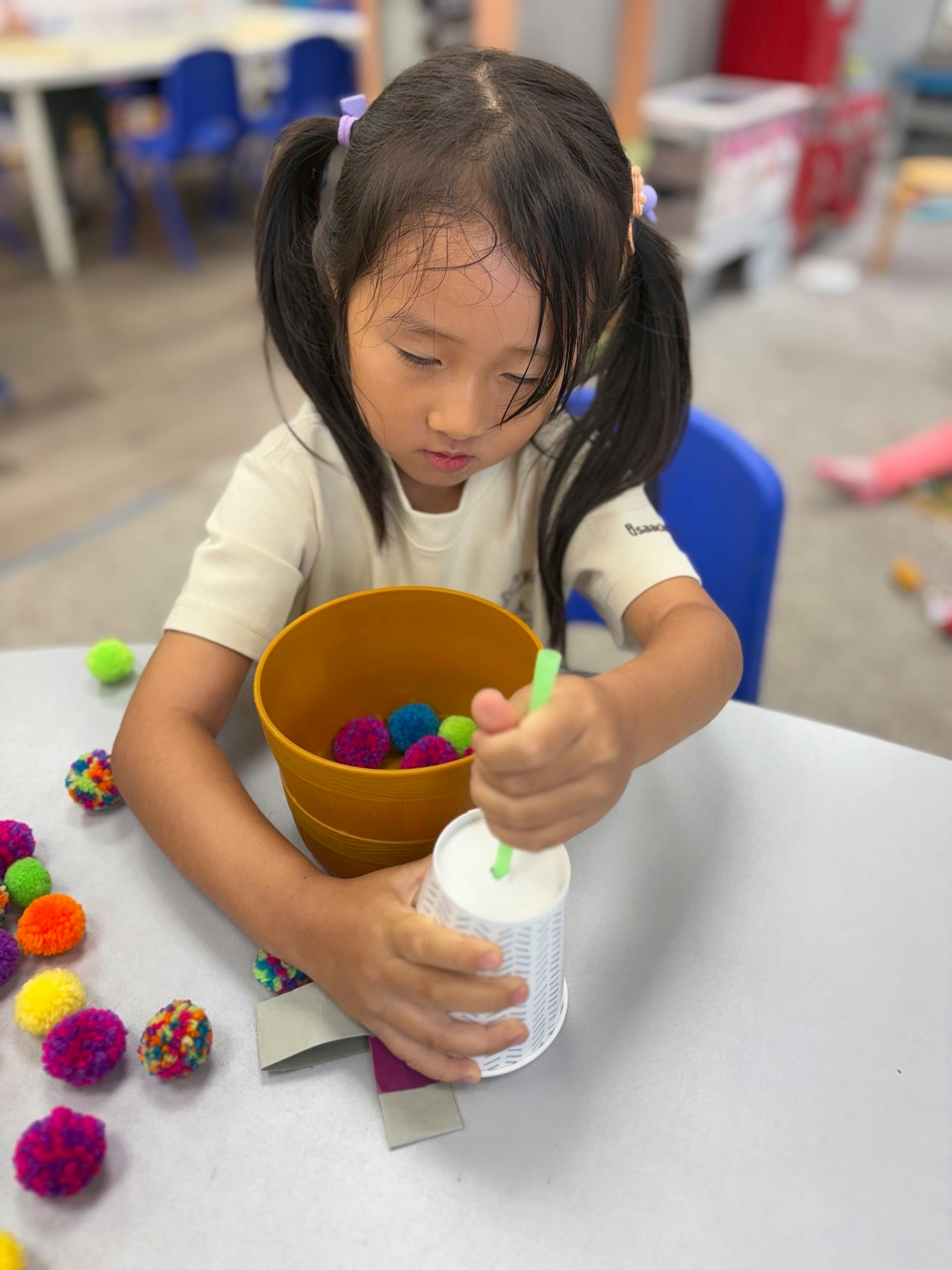Child placing a small pom-pom into a cup with a straw