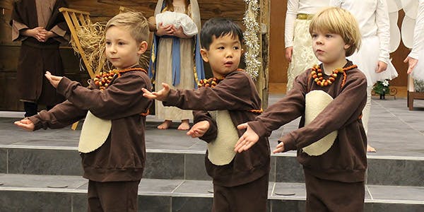Three children in brown costumes with arms outstretched