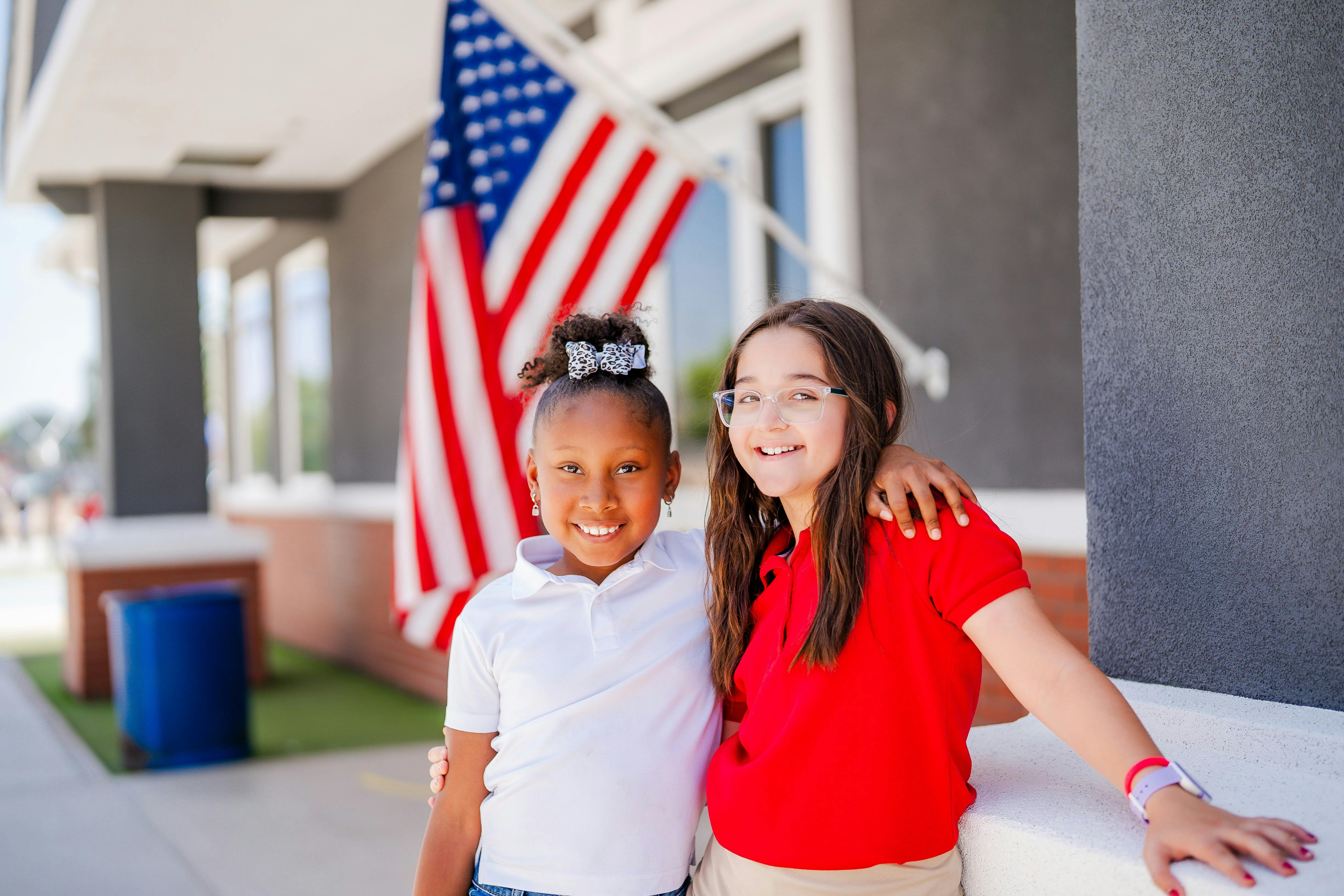 Two children standing together with an American flag in the background