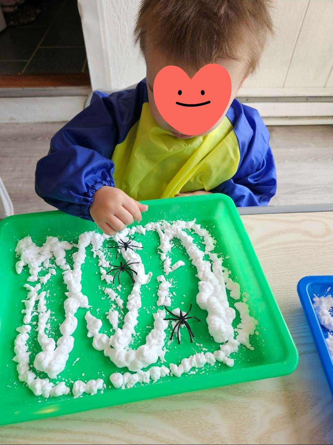 Child wearing a smock playing with toy spiders in white foam on a green tray