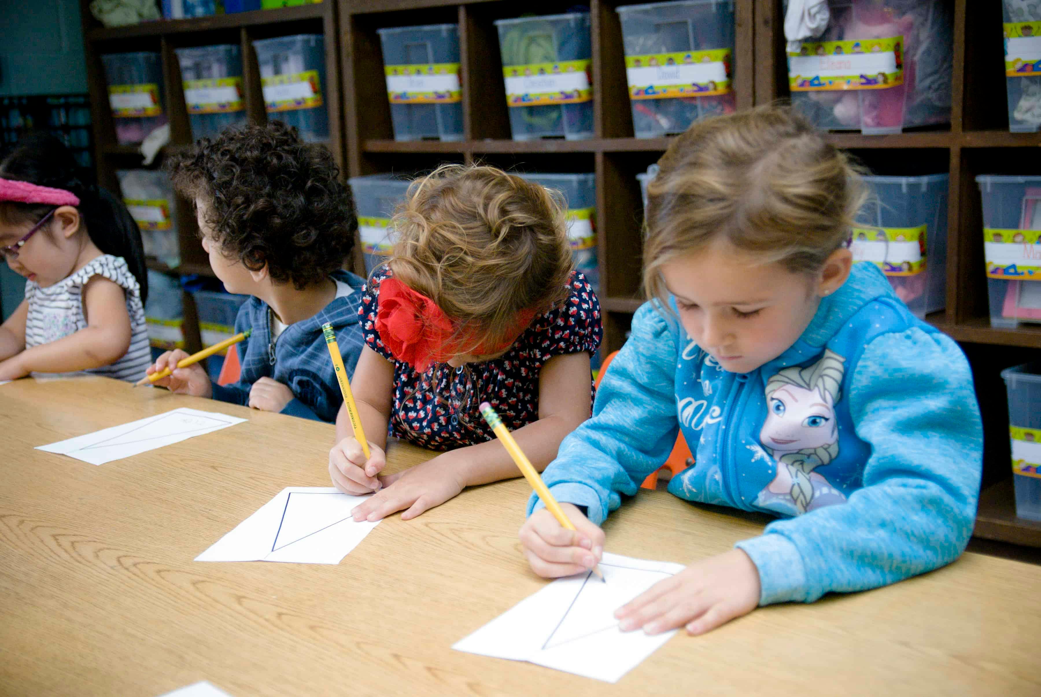 Children drawing with pencils at a table in a classroom