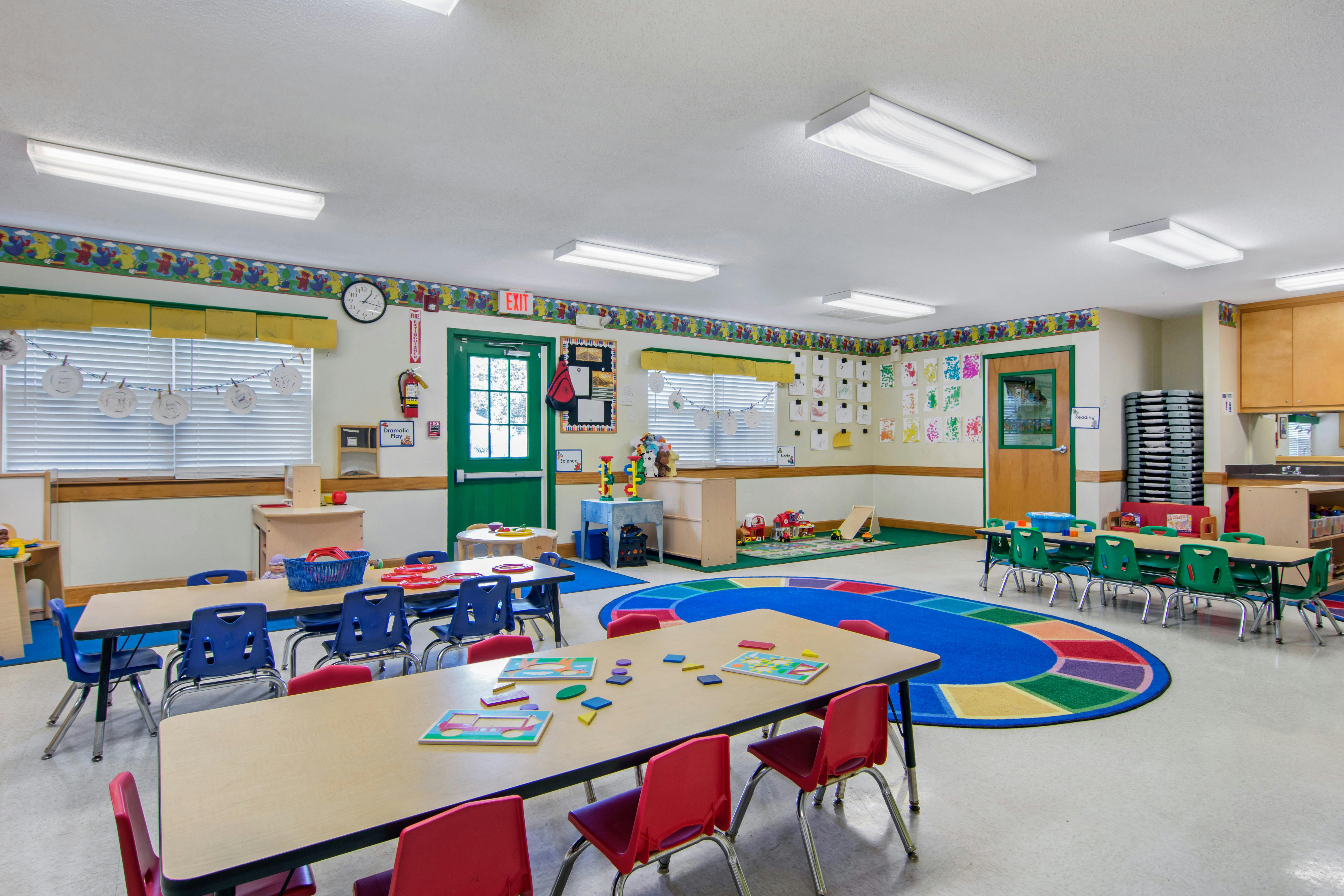 Classroom with child-sized tables and chairs, colorful rugs, and learning materials