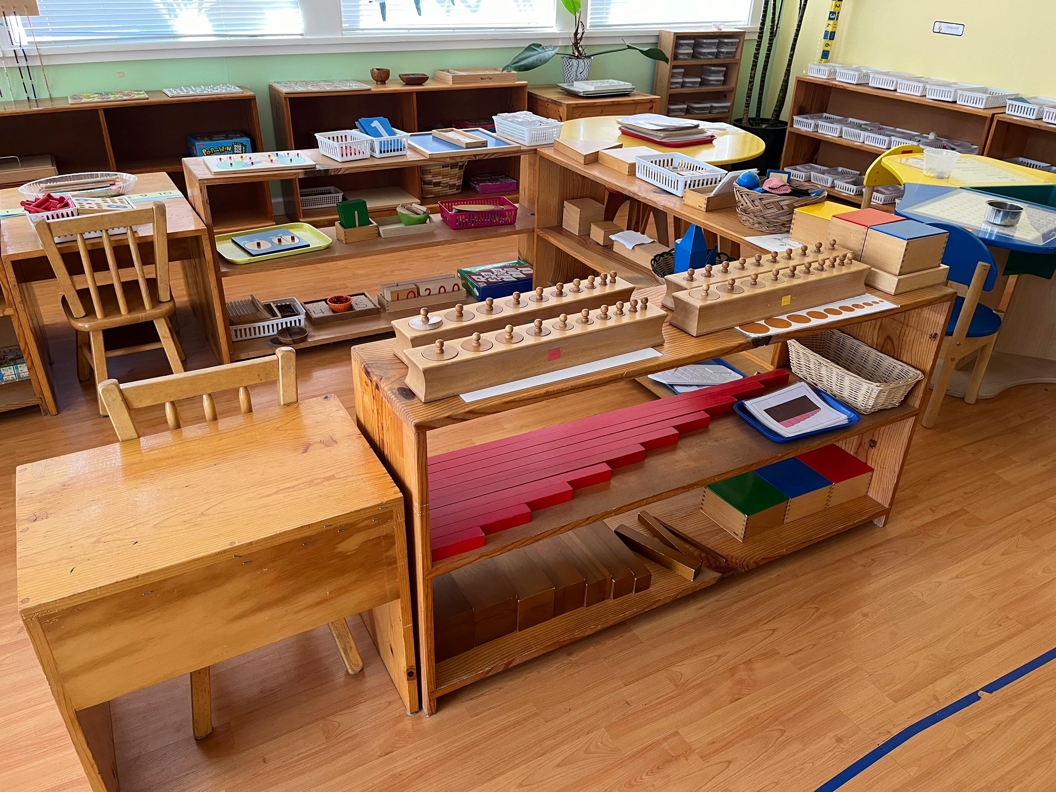 Classroom with wooden shelves, tables, chairs, and learning materials