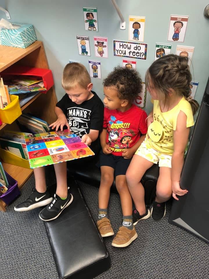 Three children sitting together looking at a colorful book