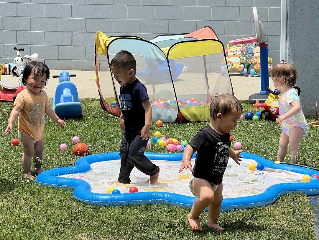 Three children playing in a splash pad with colorful balls in a grassy yard