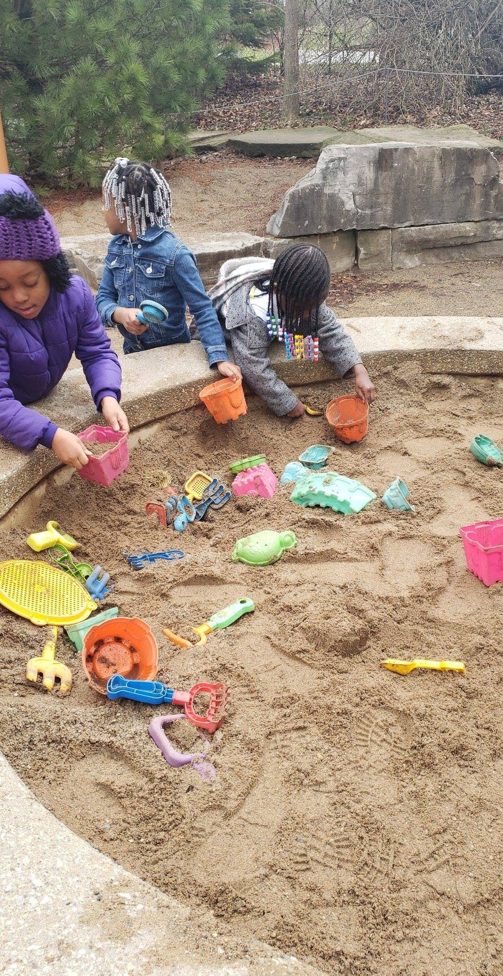 Three children playing in a sandbox with toys