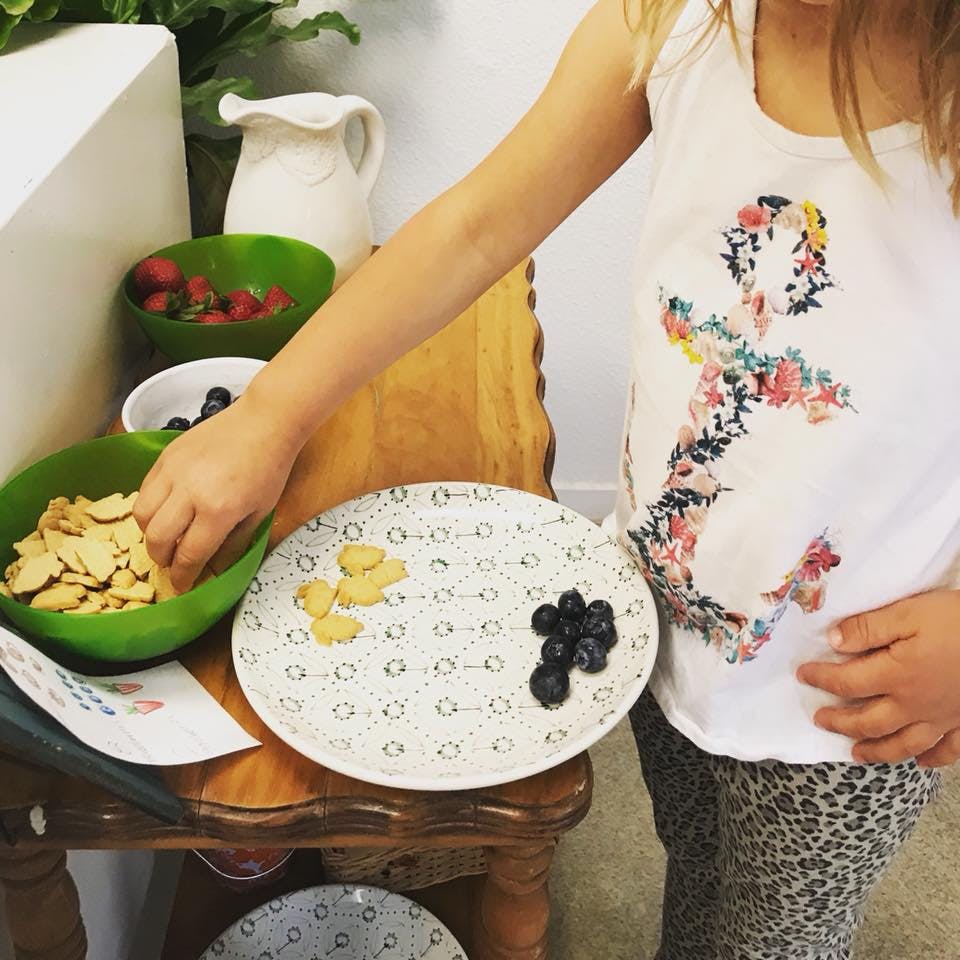 Child's hand reaching into a bowl of crackers next to a plate of blueberries