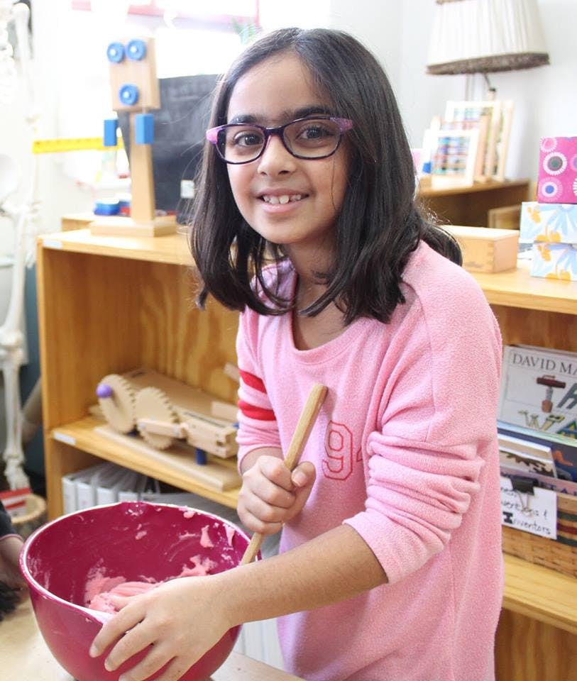 Child mixing contents in a bowl with a wooden spoon