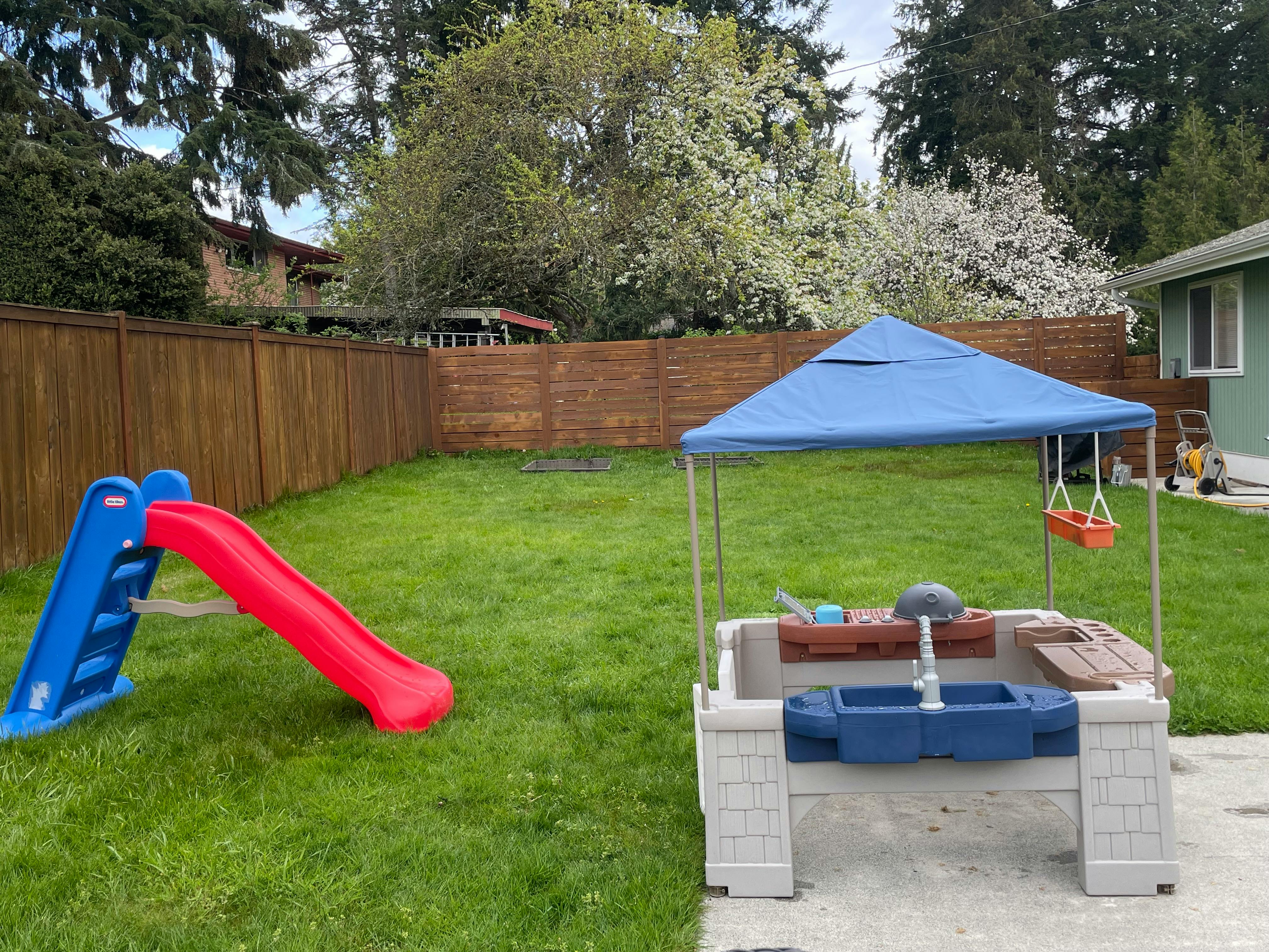 Red and blue slide and a play table with a blue canopy in a backyard