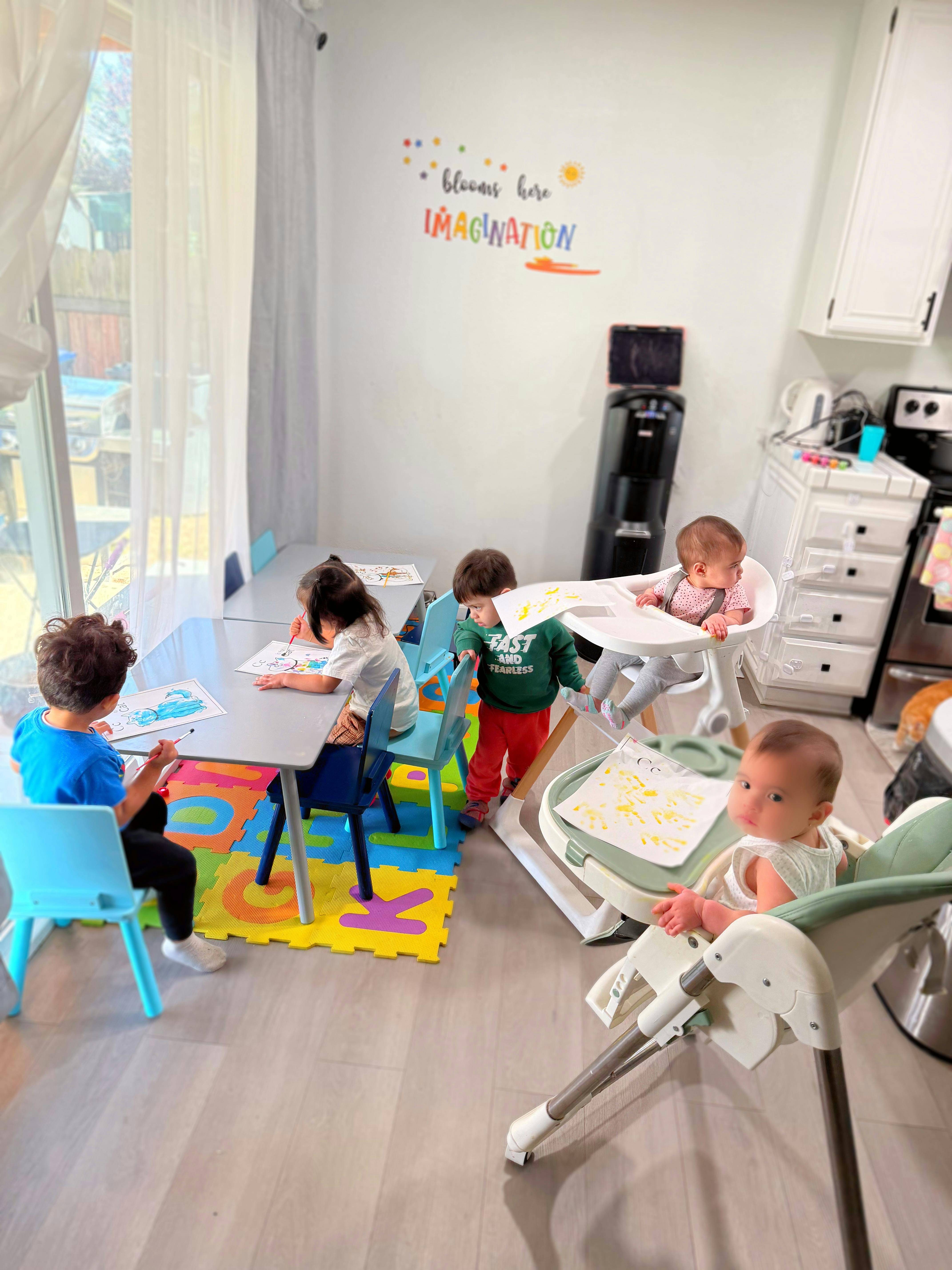 Children painting at a small table and babies in high chairs