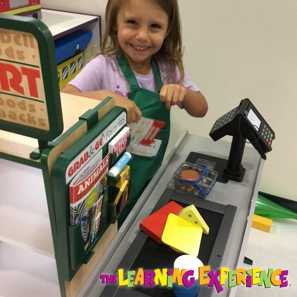 Child in an apron playing at a toy grocery store checkout