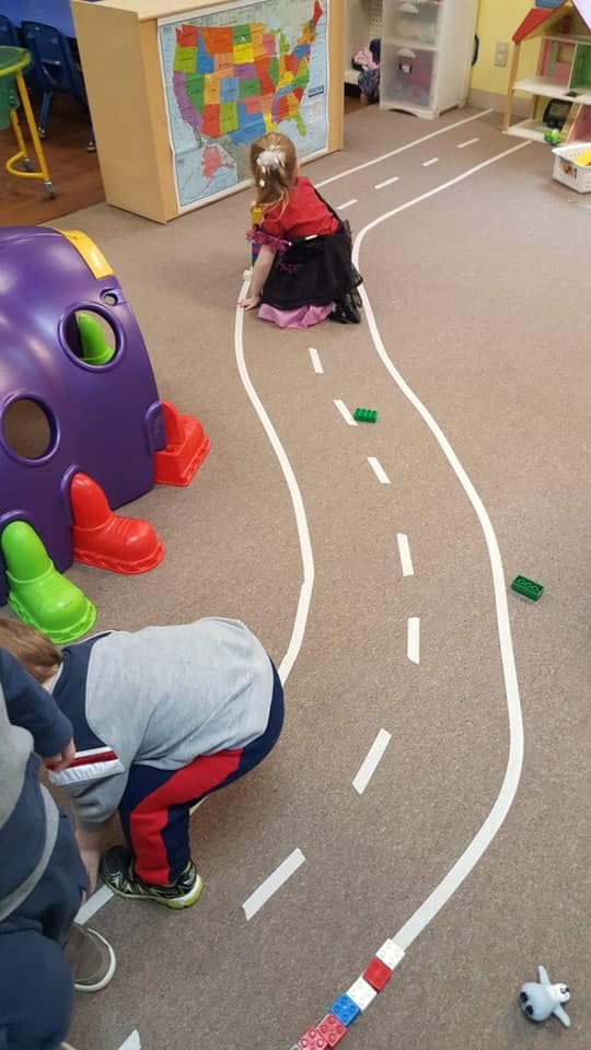 Child playing on a road-patterned rug in a classroom