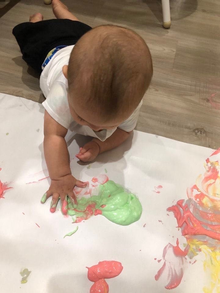 Child on floor playing with green and pink paint