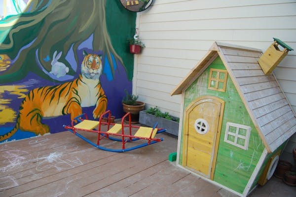 Playhouse and seesaw on a wooden deck next to a painted mural