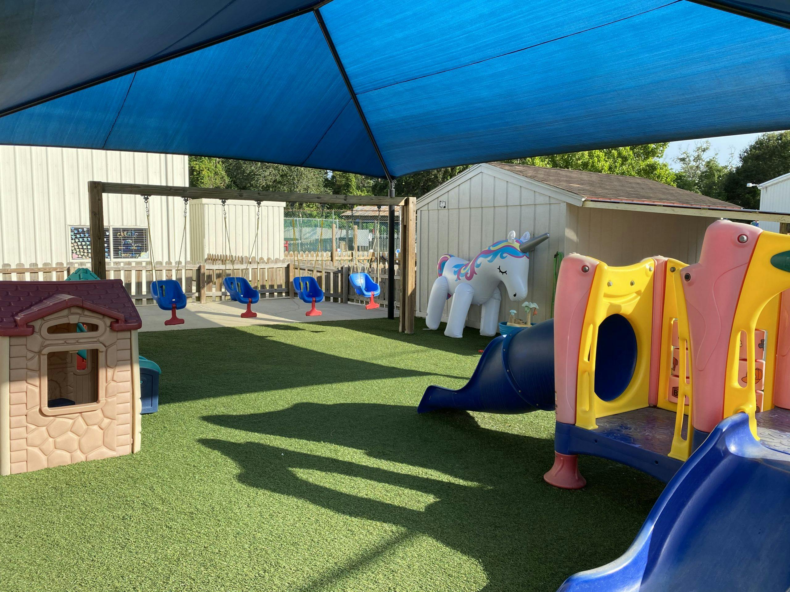 Playground with swings, playhouse, slide, and inflatable unicorn on artificial grass