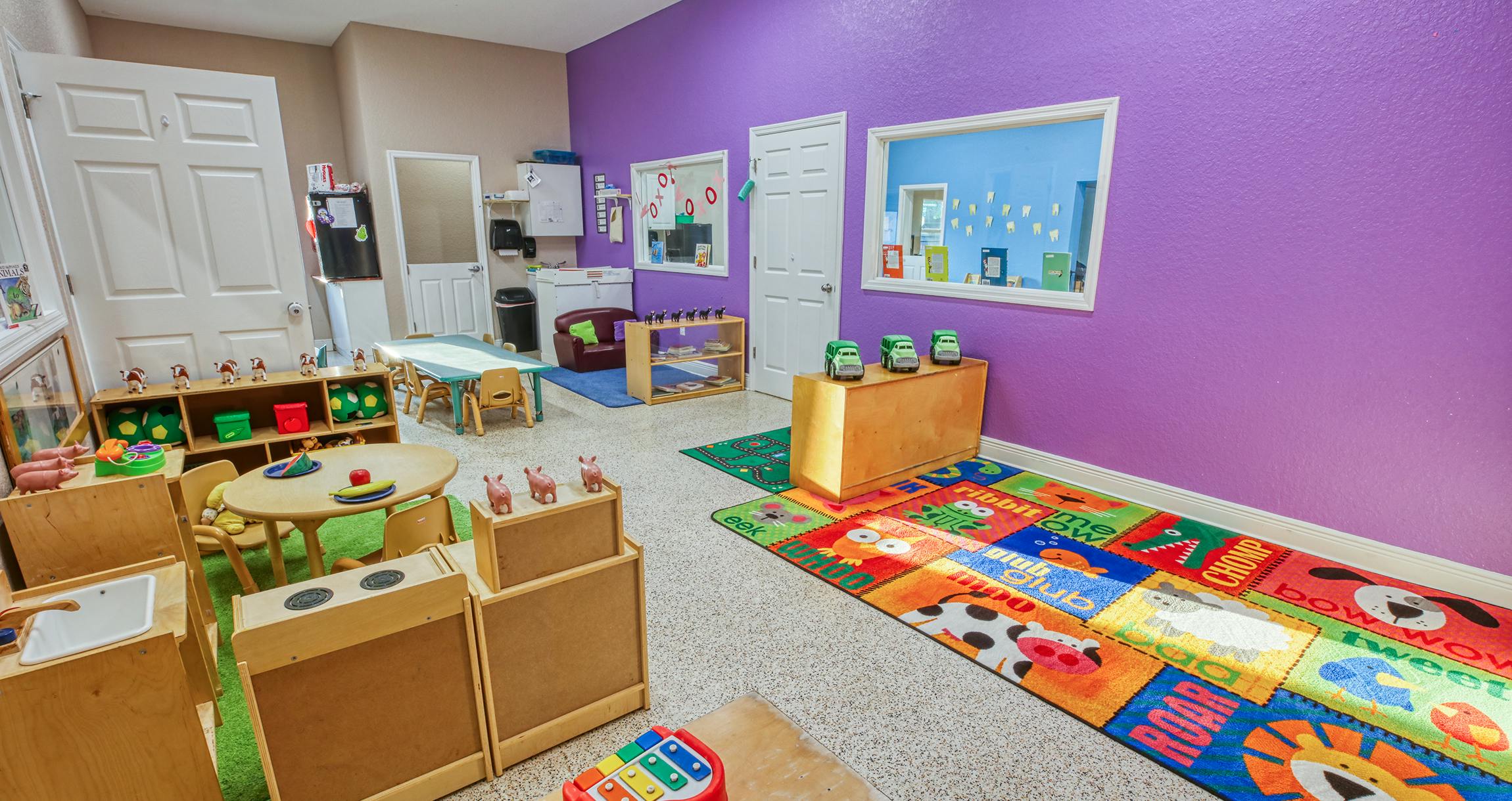 Children's classroom with purple walls, small tables, and play kitchen items