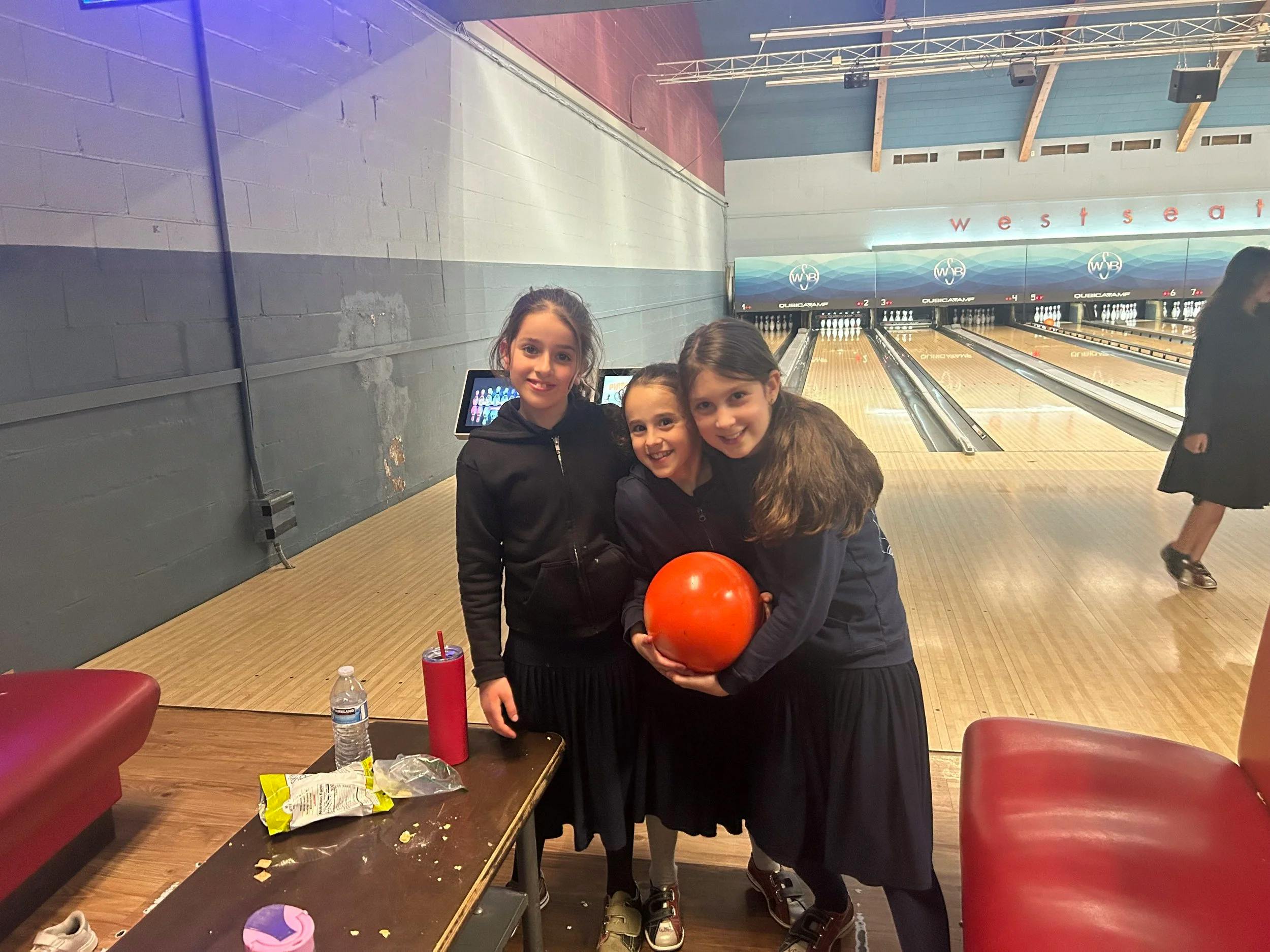 Three children smiling and posing with a bowling ball in a bowling alley