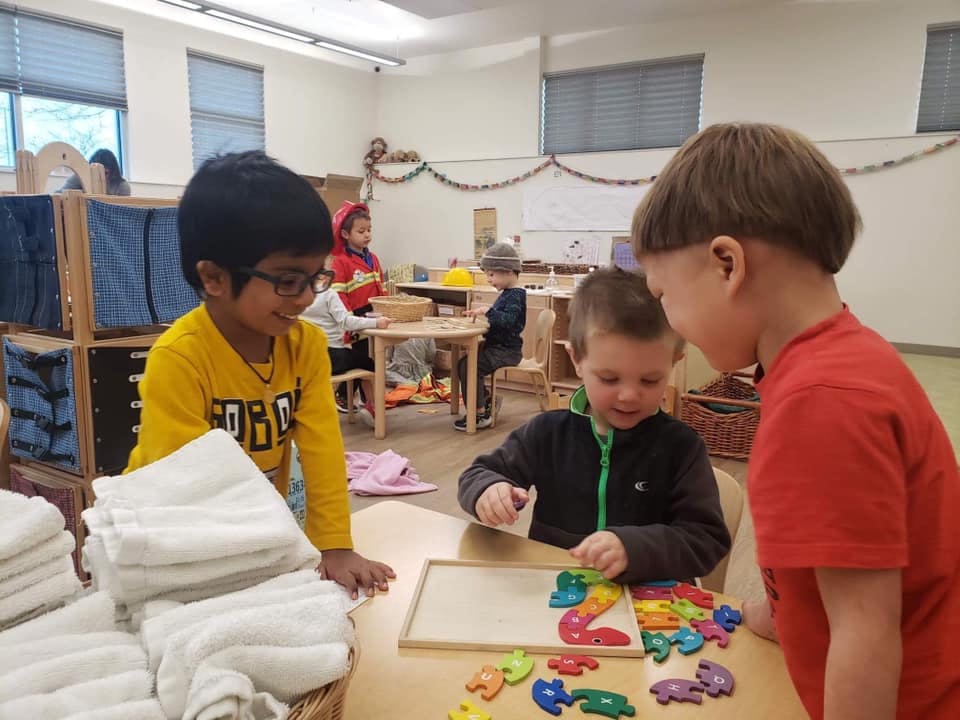 Three children playing with puzzles at a table in a classroom