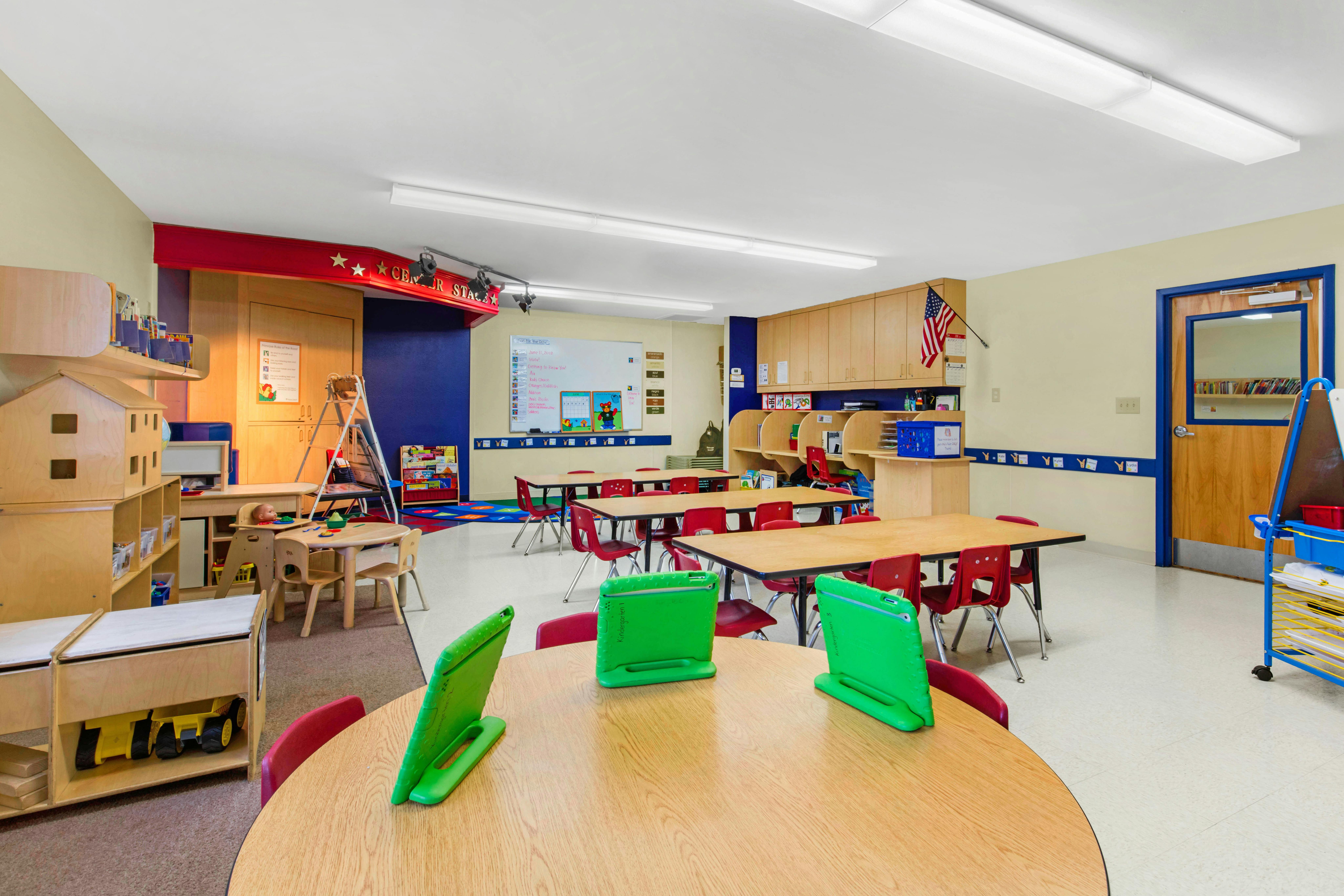 An empty early childhood classroom with multiple tables, chairs, and shelves