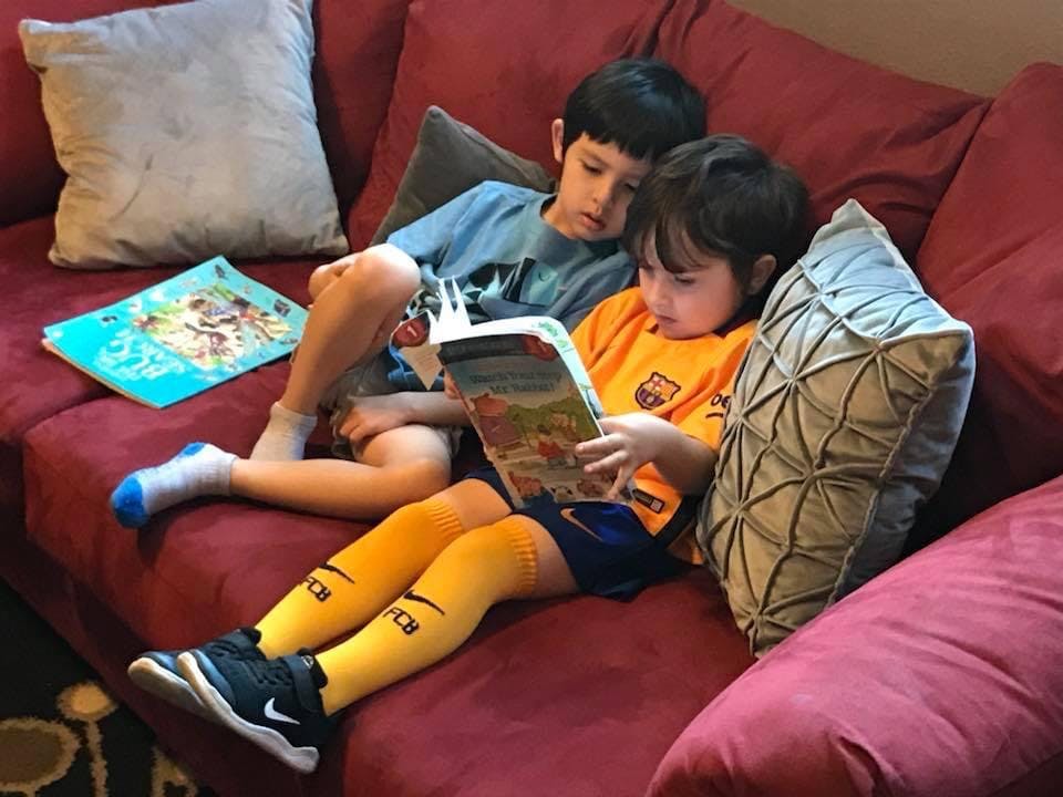 Two children reading books on a red couch
